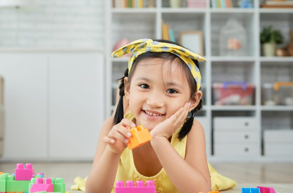 Playing girl Portrait of smiling little girl lying on floor and playing with cubes